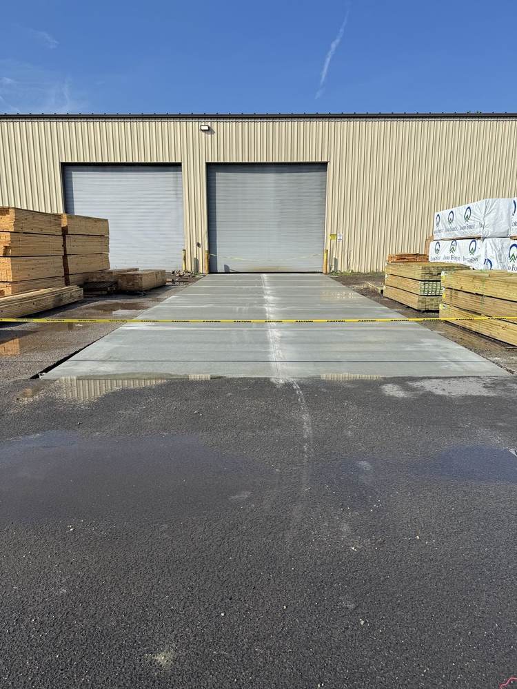 Fresh commercial concrete pad installed by South Jersey Construction Enterprise at a lumber yard building, curing behind caution tape