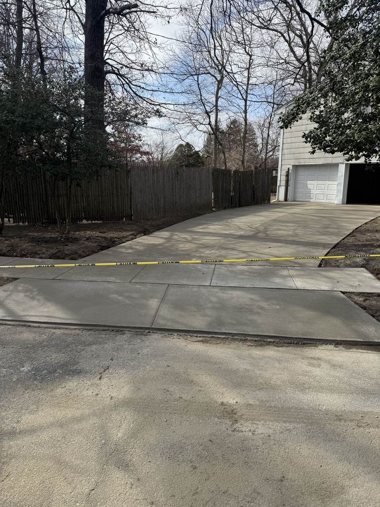 New concrete driveway curing behind caution tape at a fenced home by South Jersey Construction Enterprise