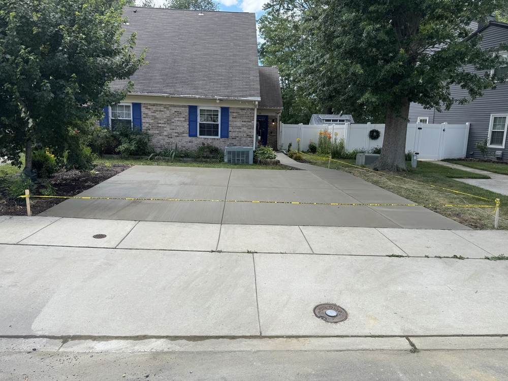 New concrete driveway curing behind caution tape at a brick home, completed by South Jersey Construction Enterprise