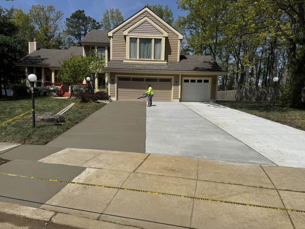 Concrete driveway with a worker finishing a new section beside existing concrete, by South Jersey Construction Enterprise
