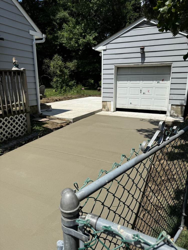 Long fresh concrete driveway installed by South Jersey Construction Enterprise beside a house, crew member spraying in background