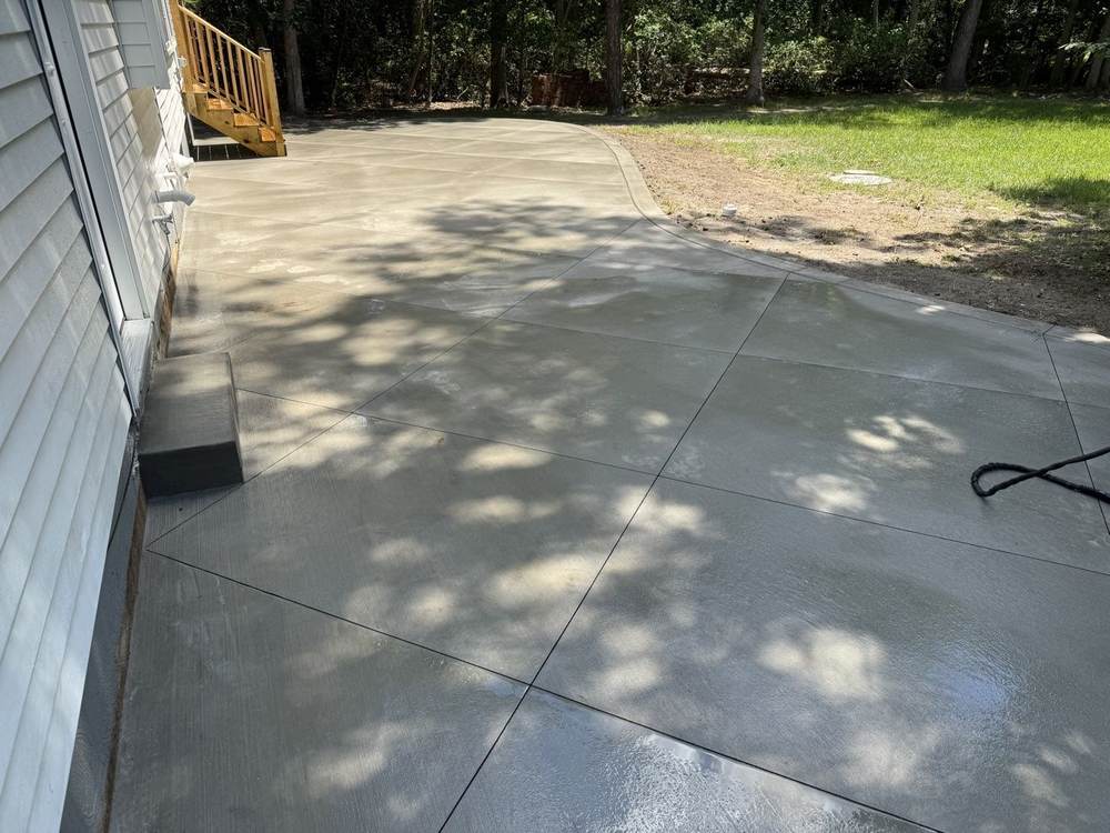 Curved concrete patio poured beside a deck with stairs by South Jersey Construction Enterprise