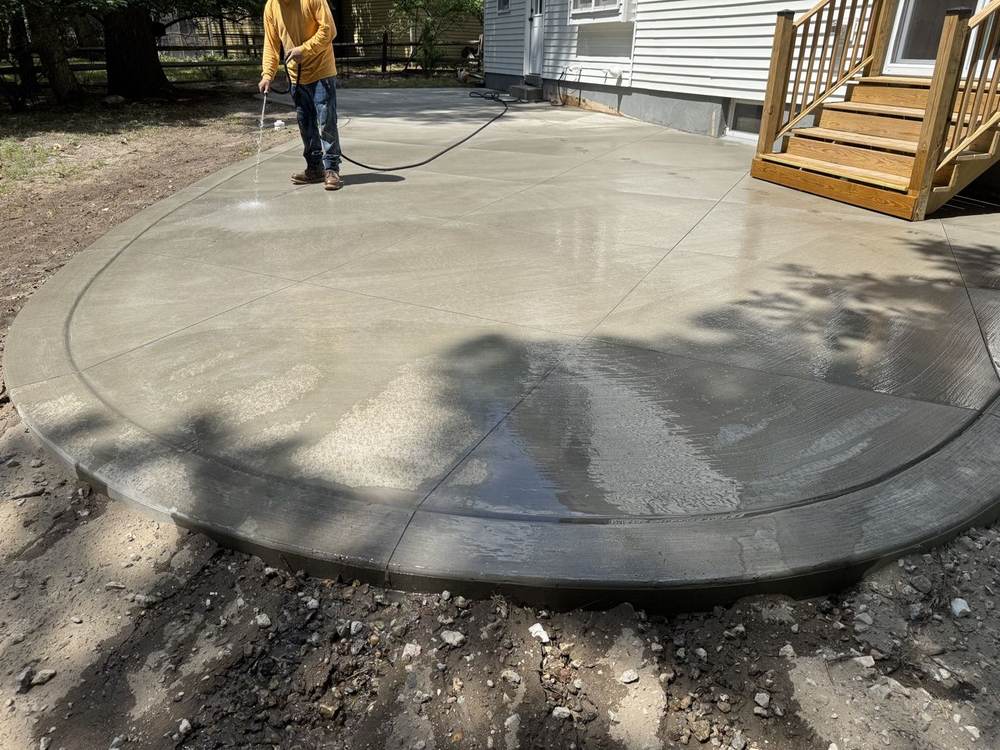 Worker watering a freshly finished curved concrete patio for South Jersey Construction Enterprise