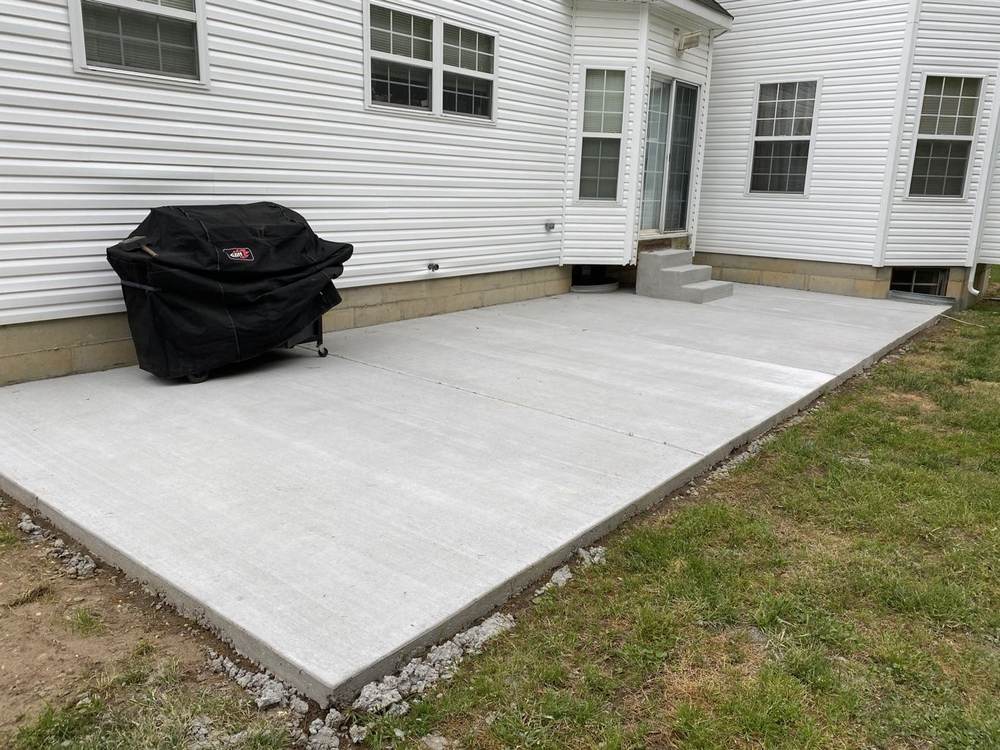 New concrete patio installed by South Jersey Construction Enterprise behind a white house, with a covered grill