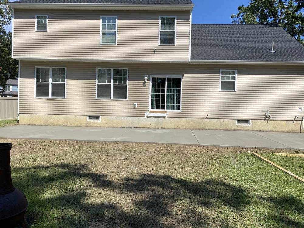 Long new concrete patio installed by South Jersey Construction Enterprise along a beige house, with a chiminea in the foreground