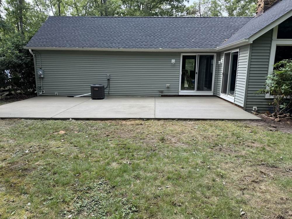 Concrete patio behind a home with sliding glass doors by South Jersey Construction Enterprise
