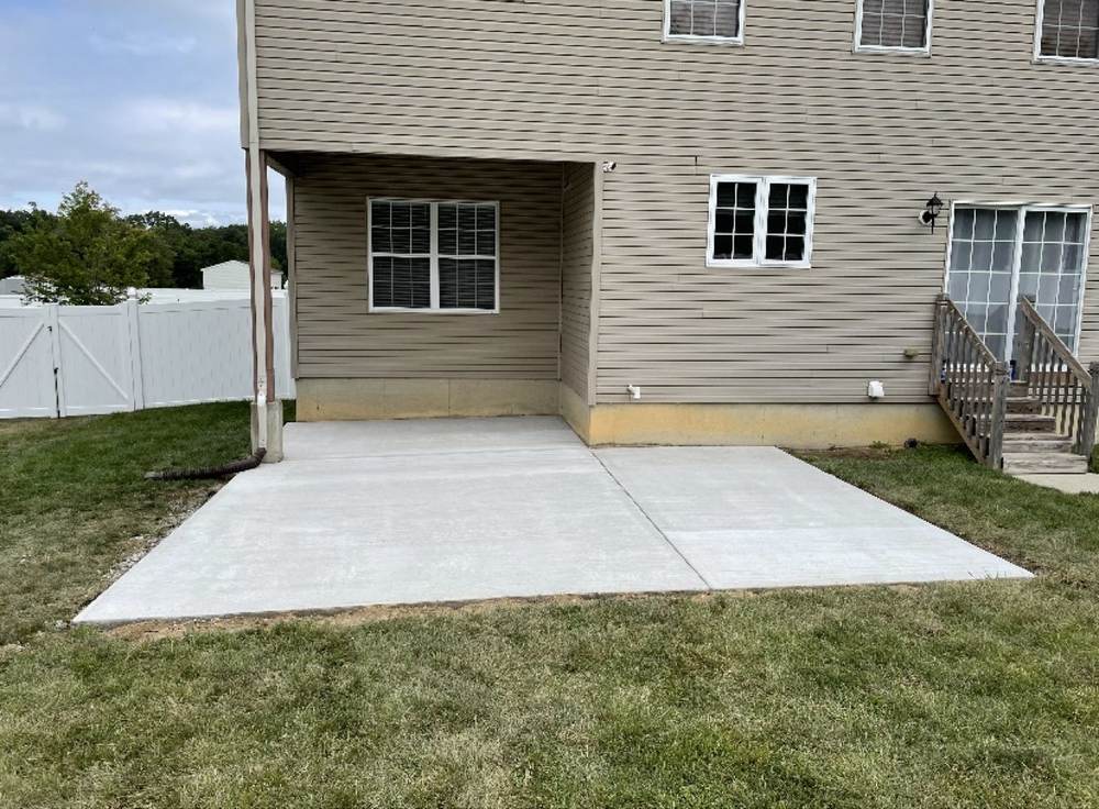 New concrete patio installed by South Jersey Construction Enterprise behind a beige house, under a deck