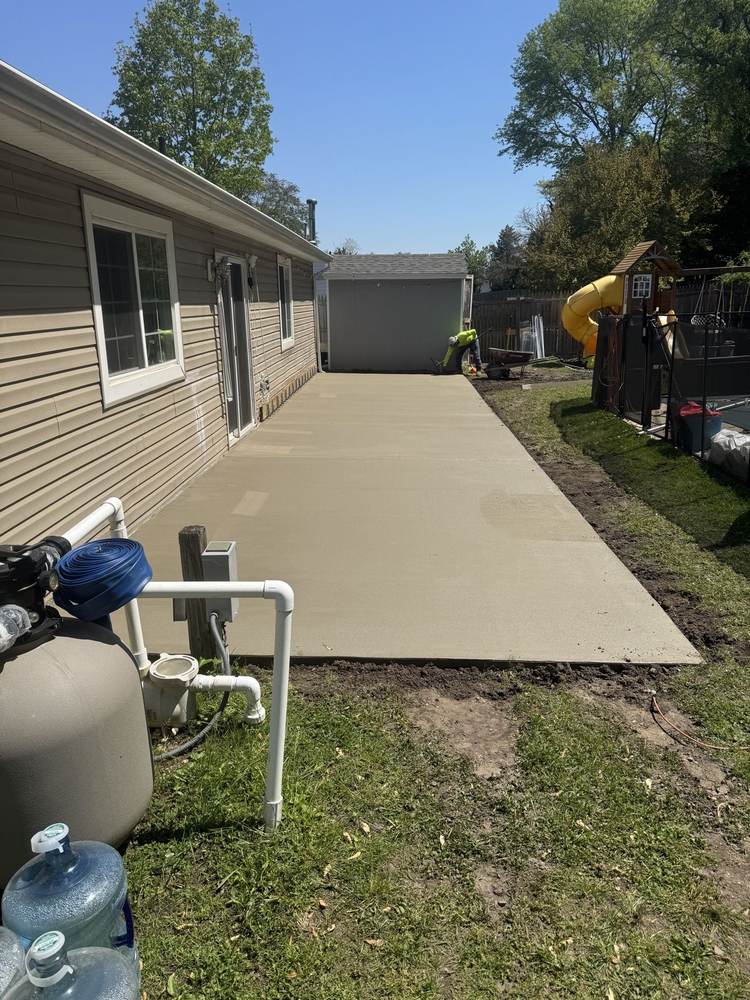 Long concrete patio beside a house with a worker edging in the background, by South Jersey Construction Enterprise
