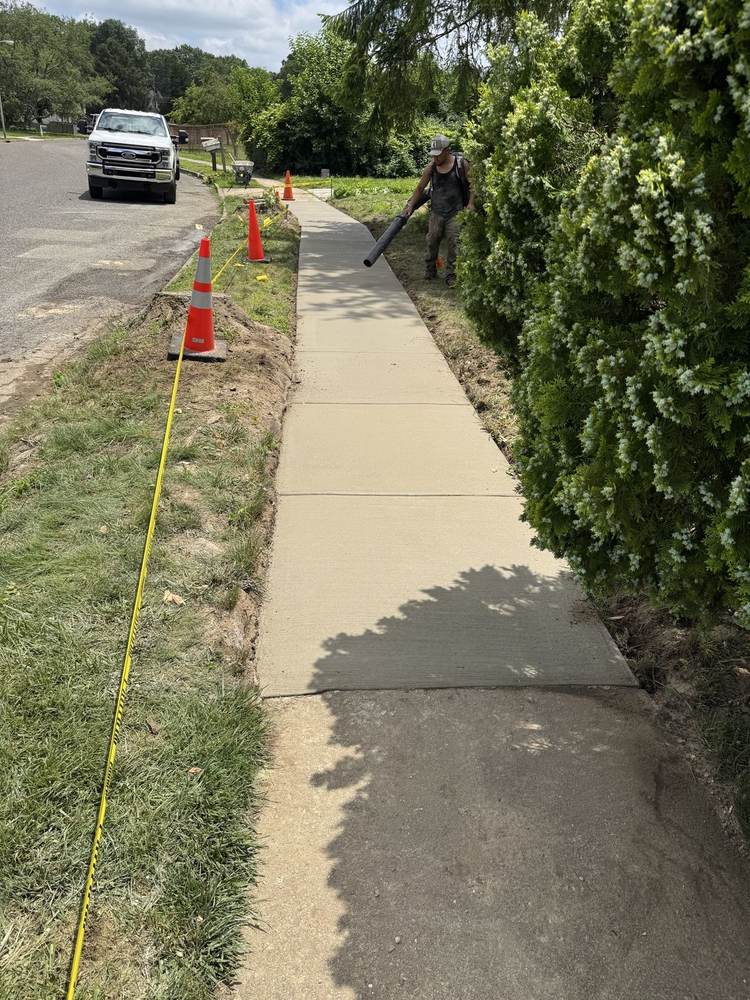 Crew member blowing debris off a new concrete sidewalk for South Jersey Construction Enterprise