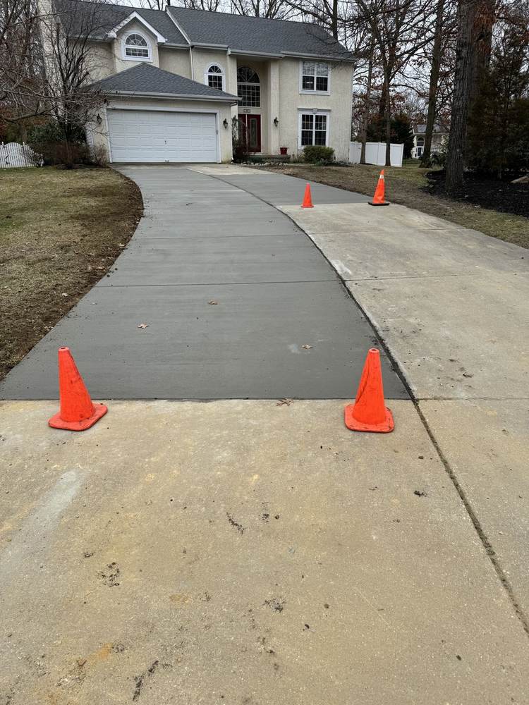 Fresh concrete sidewalk installed by South Jersey Construction Enterprise beside a house, with the dated stamp worked into the concrete