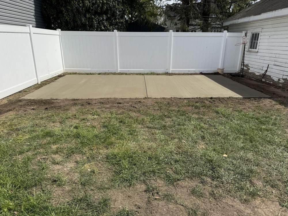 Concrete slab pad in a fenced backyard with a white vinyl fence by South Jersey Construction Enterprise