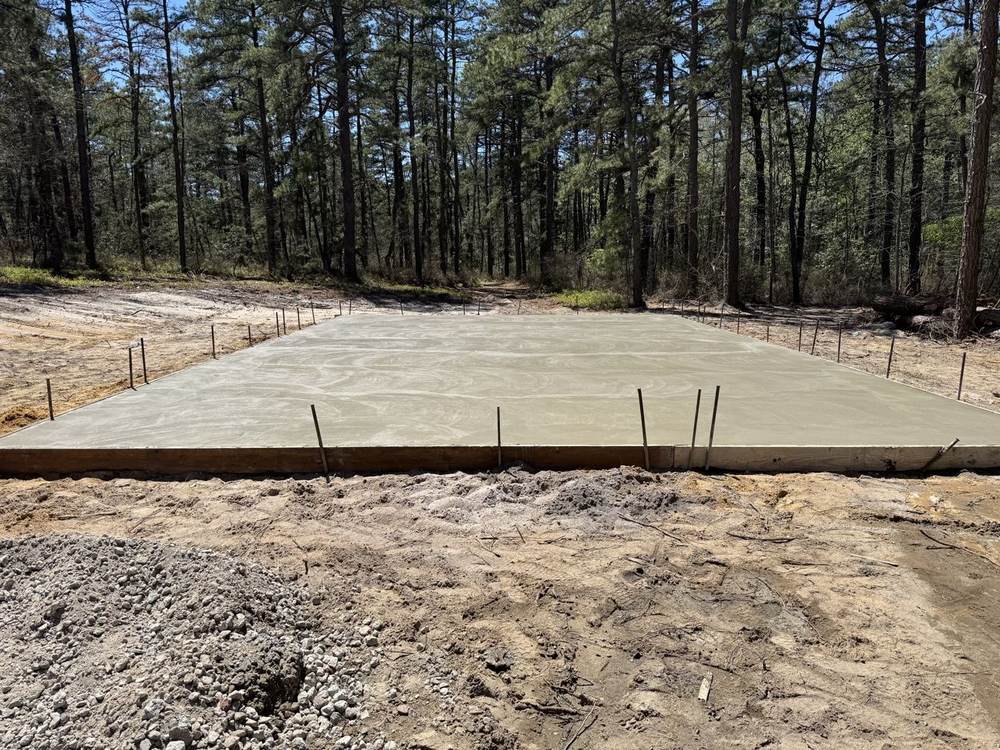 Fresh concrete slab poured in a wooded lot by South Jersey Construction Enterprise, forms still in place