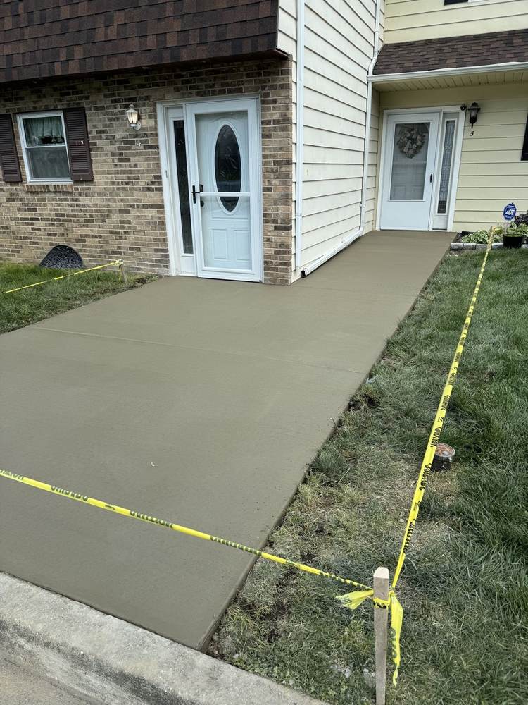 Fresh concrete walkway installed by South Jersey Construction Enterprise to a townhouse entrance, curing behind caution tape