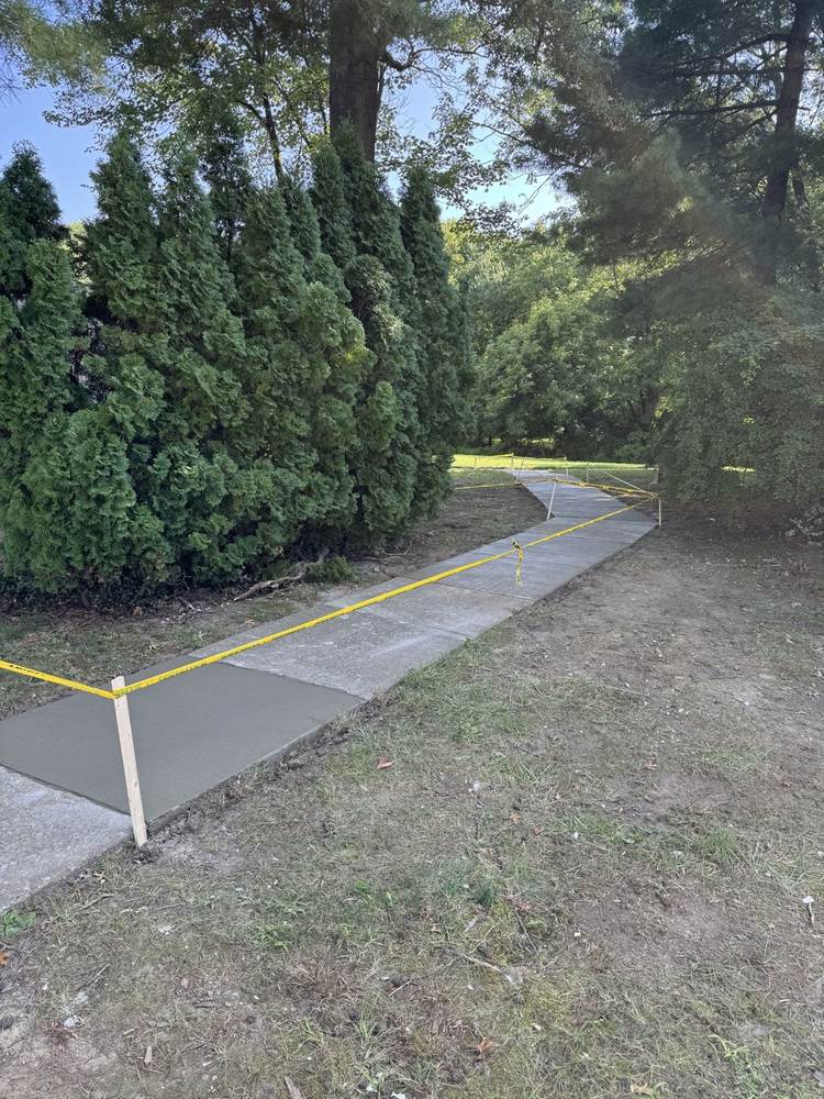 Curved concrete walkway winding through a wooded yard, roped off with caution tape while curing by South Jersey Construction Enterprise